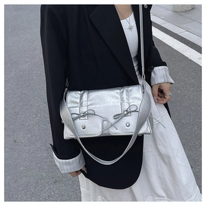 Outdoor street style view of silver square crossbody bag with bow accents and metal texture