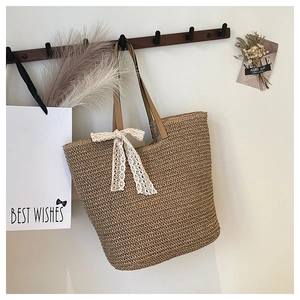 Detail of hand-woven straw tote bag with white lace bow and brown faux leather handles