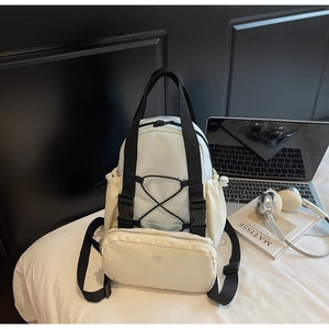 Detail of color-block backpack with detachable pouch and elastic cords on white bedding