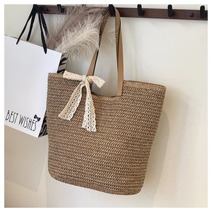 Detail of hand-woven straw tote bag with brown leather handles and white lace bow decoration