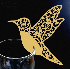 Detailed laser-cut gold hummingbird place card with heart patterns on a glass rim