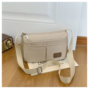 Detail view of beige nylon crossbody bag with multi-pocket zippers and adjustable strap