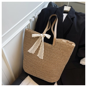 Detail of hand-woven straw tote bag featuring large lace bow and premium leather handles
