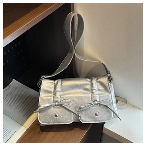 Close-up of metallic silver shoulder bag featuring dual front pockets and bow accents