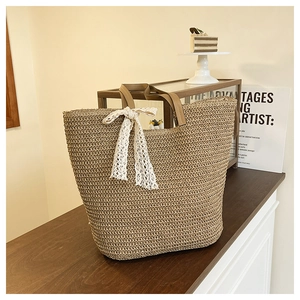 Detail of woven straw tote bag featuring brown leather handles and a white lace bow