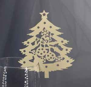 Detail of laser-cut gold Christmas tree wine glass card with intricate hollow snowflake patterns
