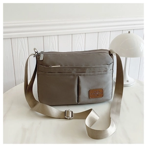 Detail of high-capacity nylon crossbody bag with multi-zipper pockets and leather logo