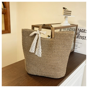 Detail of a woven straw beach tote bag with white lace bow and brown leather handles