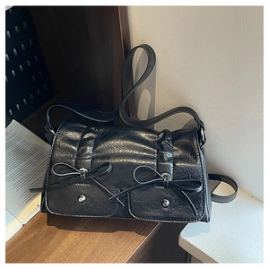 Detailed close-up of a black textured crossbody bag with decorative leather bows and metal studs