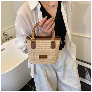Detail showing natural bamboo handle and beige straw bucket bag with leather trim