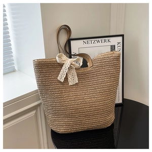 Detail of hand-woven straw tote bag featuring a white lace bow and brown leather handles