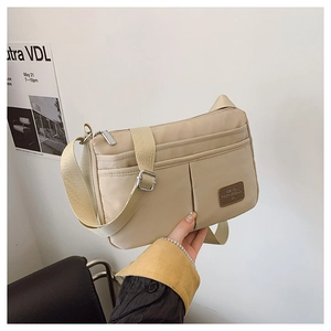 Detail view of beige nylon crossbody bag featuring multi-pocket design and leather logo tag