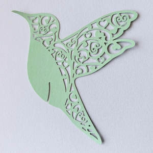 Macro shot of laser-cut light green hummingbird decoration with heart and swirl patterns