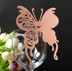 Close-up of laser-cut butterfly place card in coral pink on a glass rim for weddings