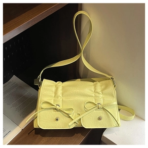 Detail of light yellow textured crossbody bag featuring decorative bows and retro folds
