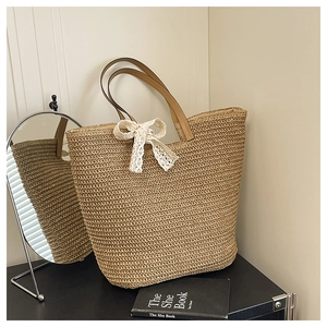 Detail of hand-woven straw tote bag with white lace bow and brown leather handles