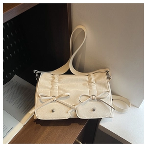 Detail view of cream crossbody bag featuring bow accents and wrinkled faux leather texture