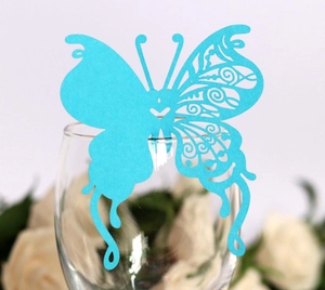 Close-up of laser-cut blue butterfly paper card on a glass rim for wedding decor