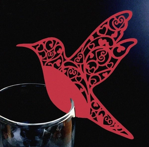 Close-up of laser-cut red hummingbird place card with heart patterns on glass