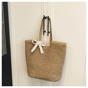 Detailed view of beige straw tote bag featuring white lace bow and brown leather handles