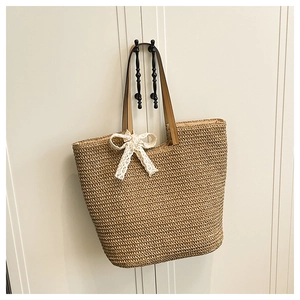 Detail of woven straw tote bag with white lace bow and brown leather handles