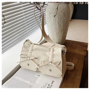 Detail of cream crossbody bag featuring decorative bows and silver metallic studs