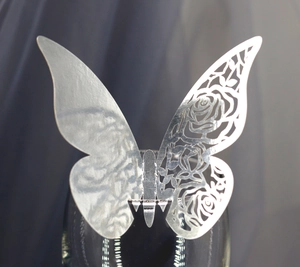 Détail d'un marque-place papillon argenté avec découpe laser rose sur rebord de verre