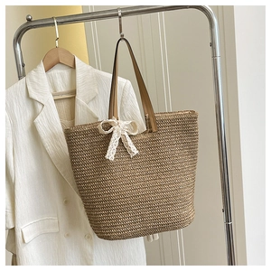 Detail of handwoven straw tote featuring a white lace bow and brown leather handles