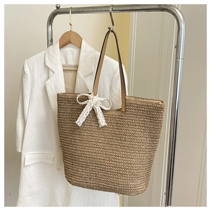 Detail of handwoven straw tote bag with elegant white lace bow and leather handle