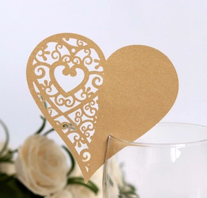 Detail of laser-cut gold heart place card on a glass with elegant white rose background