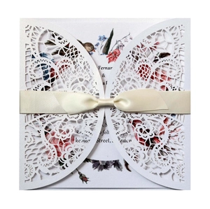 Elegant laser-cut white lace wedding invitation with a satin bow and floral inner card