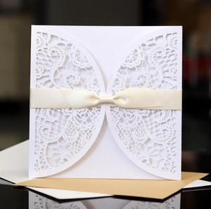 Detail of laser-cut lace invitation card featuring an elegant ivory satin ribbon bow