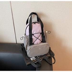 Detail of a purple and grey utility backpack with elastic cords on a black leather sofa