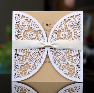 Elegant laser-cut floral wedding invitation with cream ribbon bow and kraft paper insert