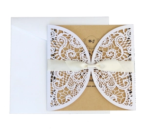 Detailed view of laser-cut lace wedding invitation with kraft insert and white ribbon