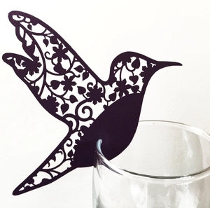 Vue détaillée d'un marque-place colibri noir découpé au laser posé sur le bord d'un verre