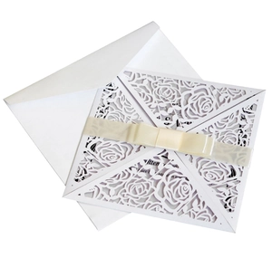 Detailed laser cut rose pattern on white wedding invitation with cream ribbon bow