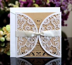Close-up of laser-cut lace wedding invitation with silk bow and kraft paper insert