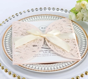 Detail of pink laser-cut wedding invitation with satin bow on a luxury porcelain plate