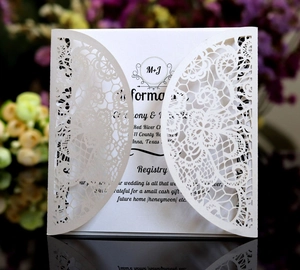 Detail of laser-cut white lace invitation card with elegant floral pattern and inner insert