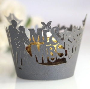 Macro shot of laser-cut Mr & Mrs paper cupcake wrapper with elegant wedding silhouette