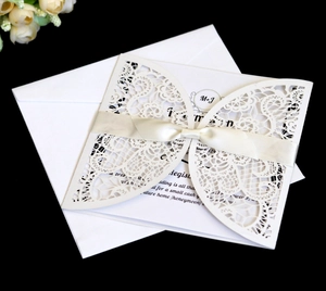 Close-up of laser-cut ivory wedding invitation set with ribbon bow and floral pattern