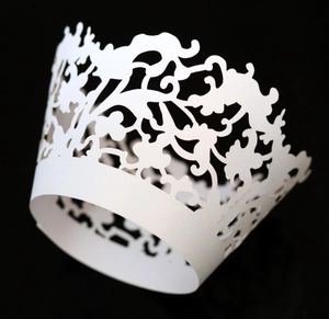 Macro detail of laser-cut white lace cupcake wrapper with ornate floral patterns