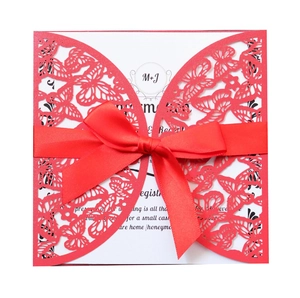 Detail of laser-cut red wedding invitation with butterfly pattern and silk bow ribbon