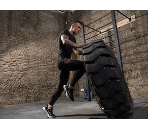 Action shot of men's compression fitness set during tire flip workout in a gym