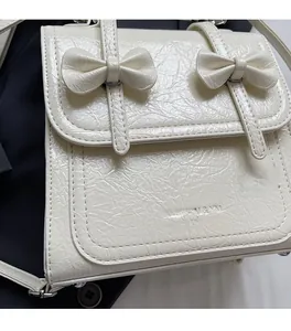 Close-up of beige wrinkled patent leather bag with decorative bows and brand embossing