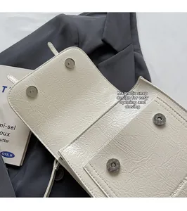 Detail of off-white pleated crossbody bag with dual magnetic snap closure on a blazer
