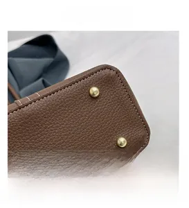 Detail of brown lychee leather tote with white stitching and gold metal protective feet