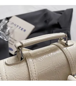 Close-up of cream-white handbag handle with glossy crinkle texture and metal ring detail