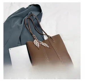Detail view of large brown tote bag capacity compared with an iPad and a smartphone